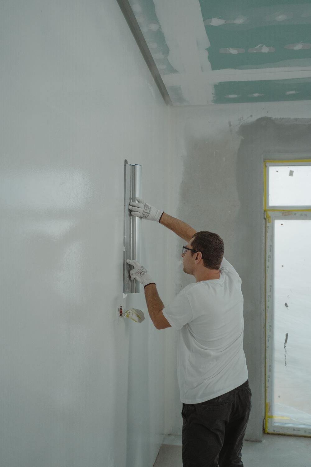 A builder smoothing a newly boarded wall with a straightedge in a house being renovated