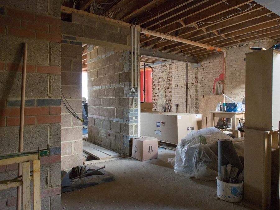 The ground floor of a house stripped back for refurbishment, with bare brick and blockwork walls, exposed ceiling joists and a new steel beam