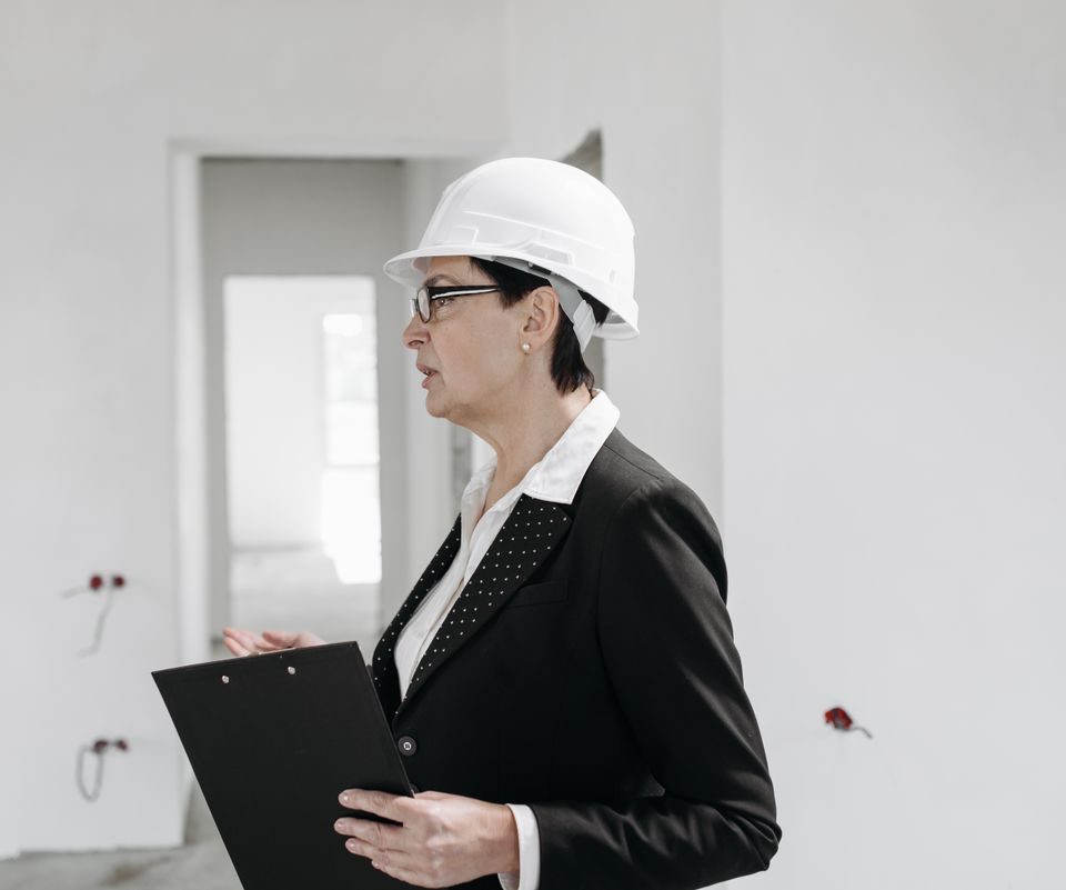 A commercial manager in a white hard hat with a clipboard walking an unfinished interior