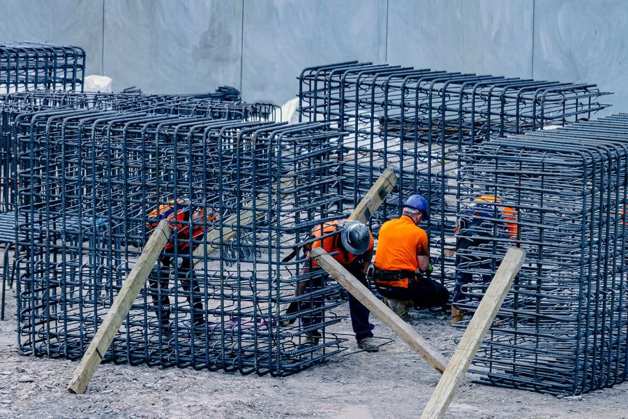 Steel fixers in hard hats and high-visibility tops tie reinforcement cages on a commercial construction site