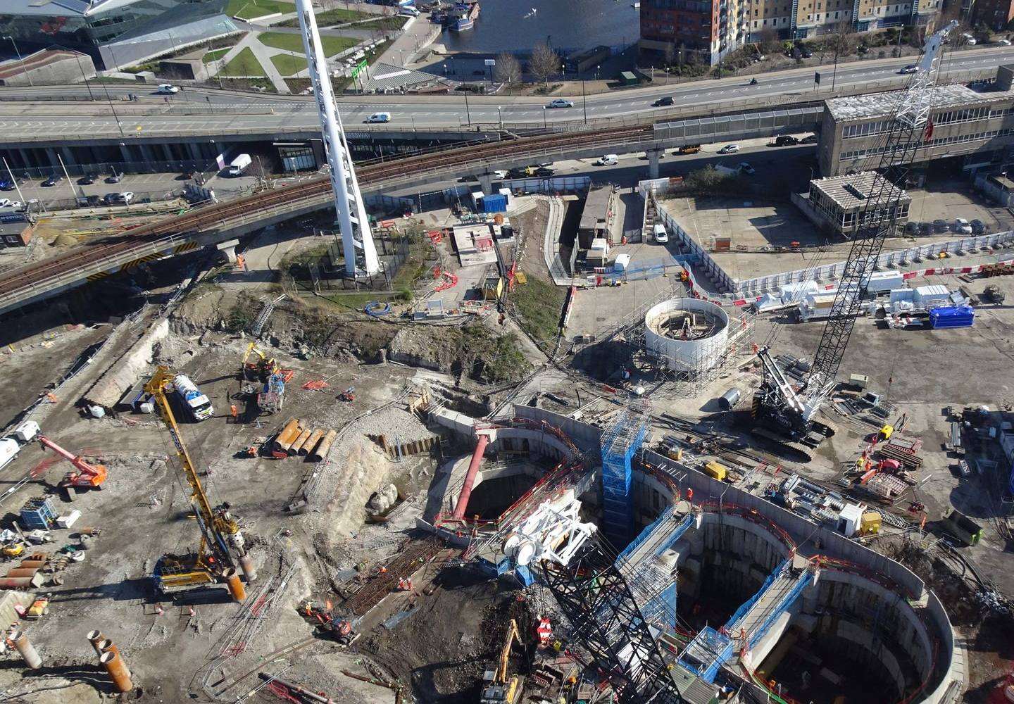 An aerial view of a large city construction site with cranes, piling rigs and a railway beside it